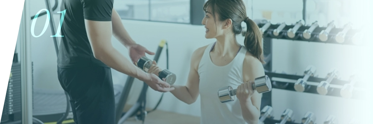 ジムでトレーナーのサポートを受けて筋トレを行う女性