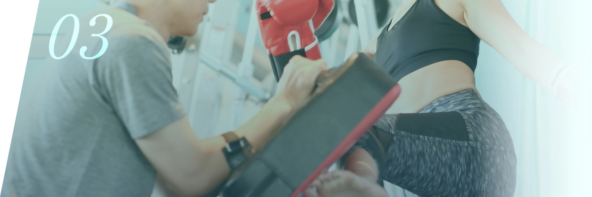 ジムでトレーナーのサポートを受けてキックボクシングを行う女性