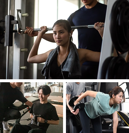 ジムで男女の利用者がトレーナーのサポートを受けながら筋トレを行う様子